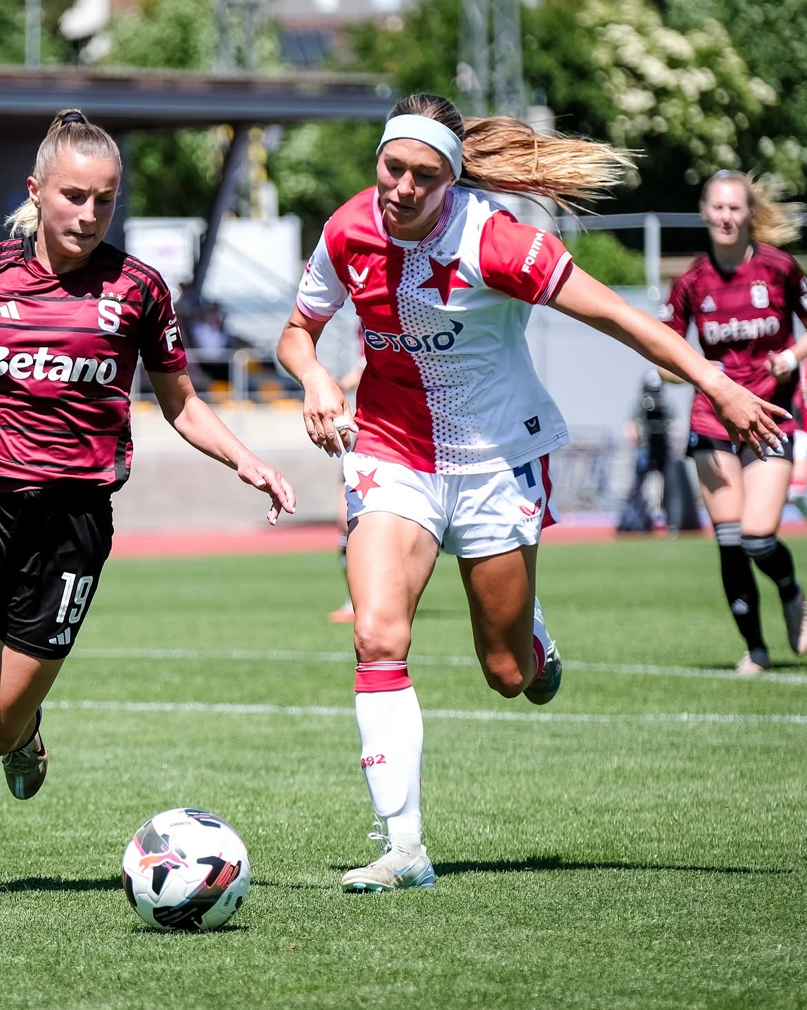 A Slavia Praha player driving the ball past a Sparta Praha opponent in a sunlit cup tie