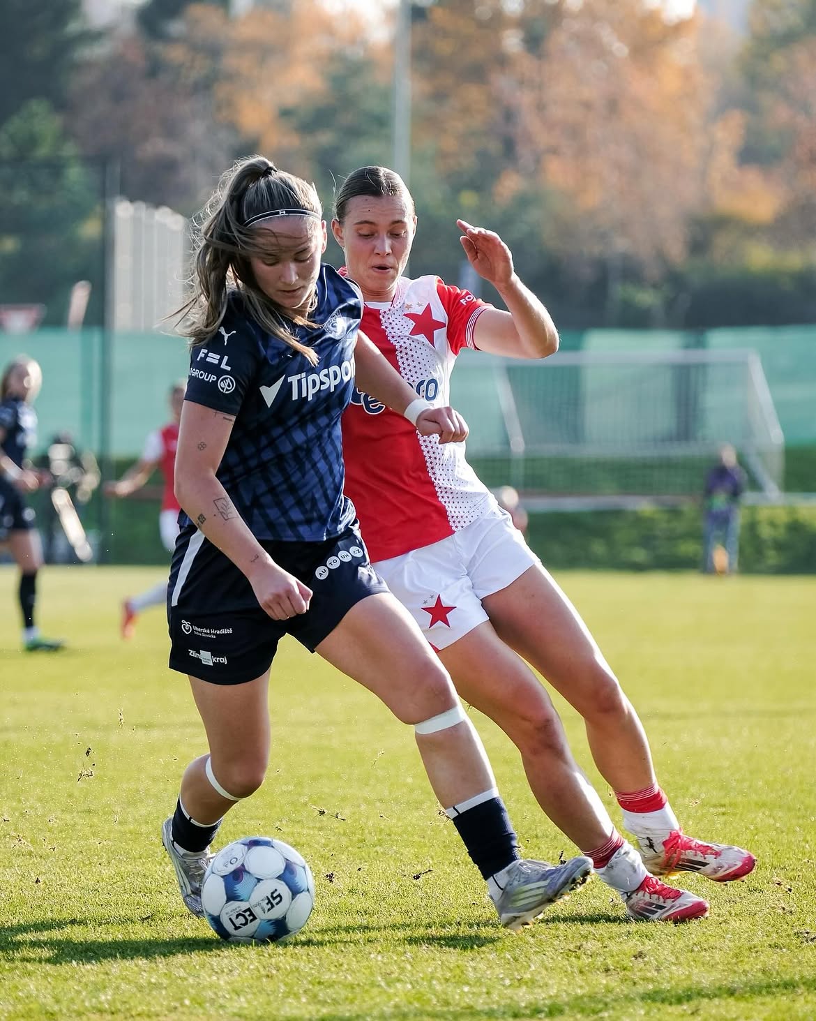 A Slovácko player shielding the ball from a Slavia Praha opponent on an autumn afternoon
